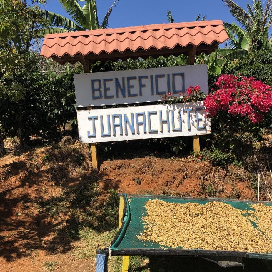 Sign for 'Beneficio Juanachute' with coffee beans on a table outdoors.