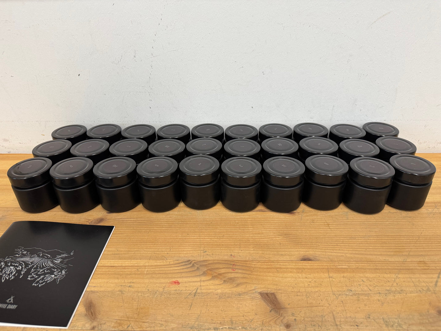 Row of black cylindrical containers containing masterpiece coffees on a wooden surface with a white background