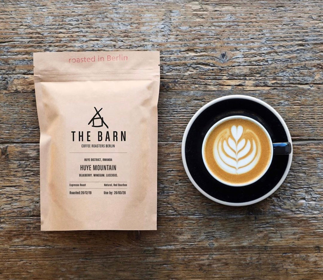 Coffee bag from 'The Barn' and a cup of coffee with latte art on a wooden surface