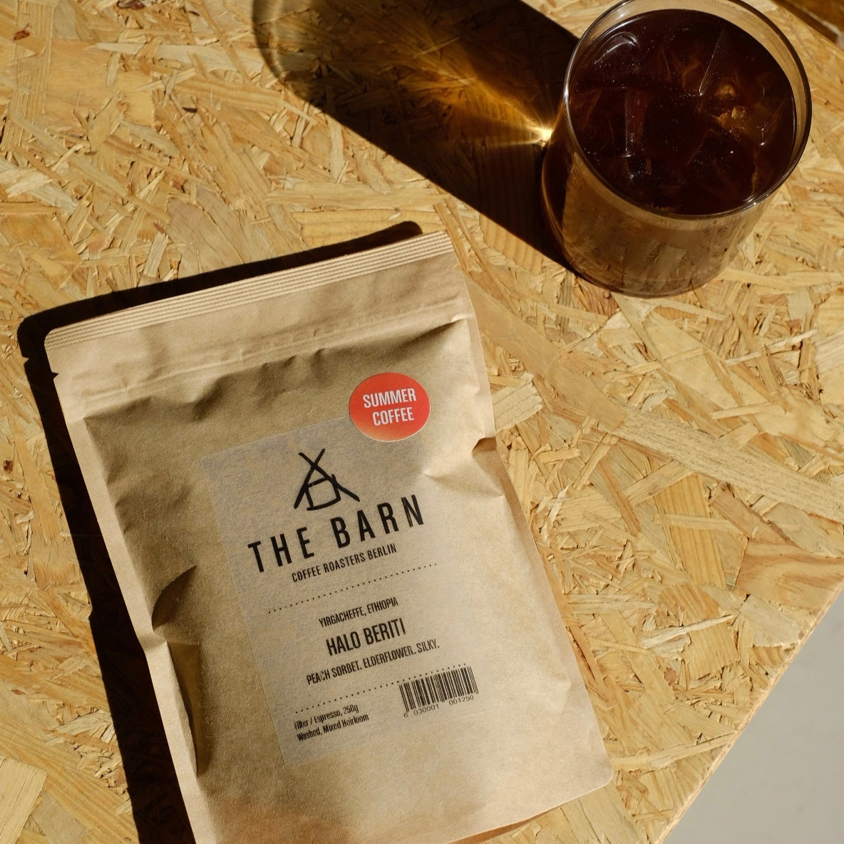 Coffee package from 'The Barn' on a wooden surface with a glass of iced coffee.