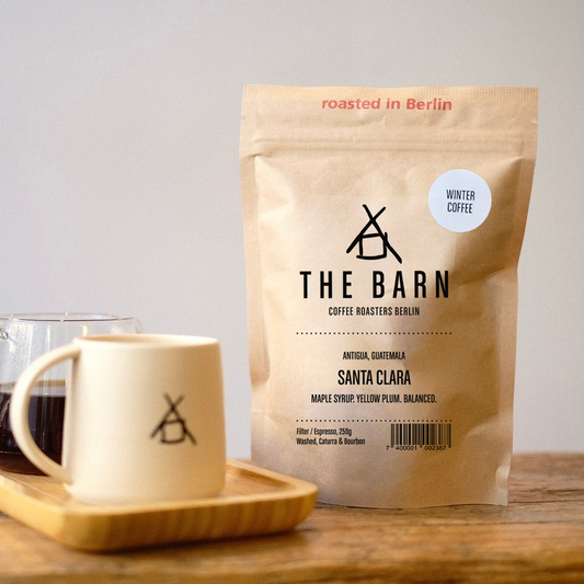 Coffee bag and mug with 'The Barn' branding on a wooden surface.