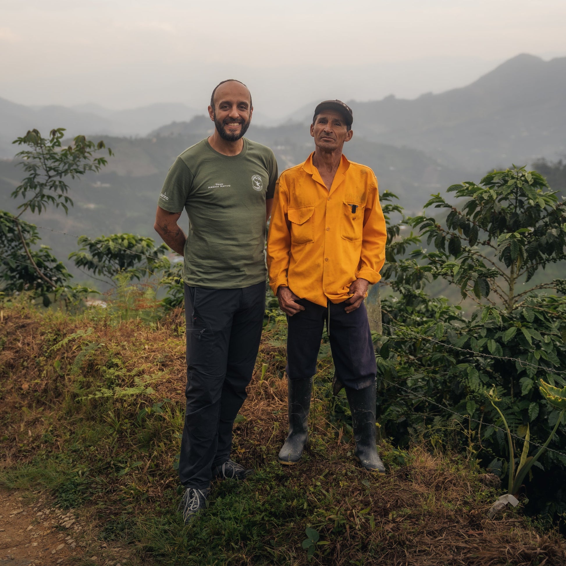 Two men standing in a mountainous landscape with greenery.