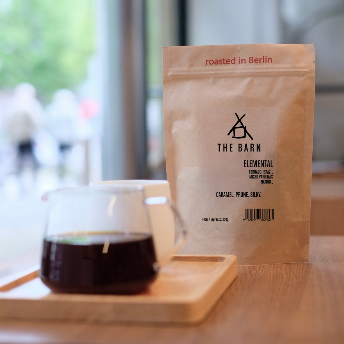 A 250 grams bag of Elemental, Brasilien Coffee on a table with a Coffee in a Server on a wooden table