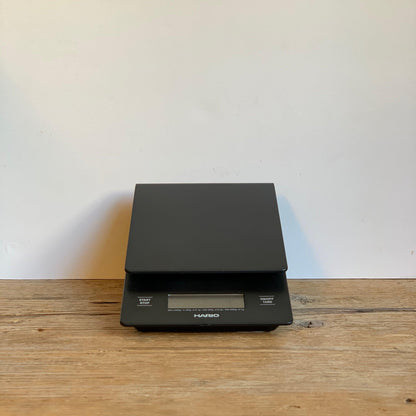 HARIO SCALE WITH BUILT IN TIMER SLIGHTLY UPRIGHT ON A WHITE WALL, PLACED ON A WOODEN TABLE  (9427968455)